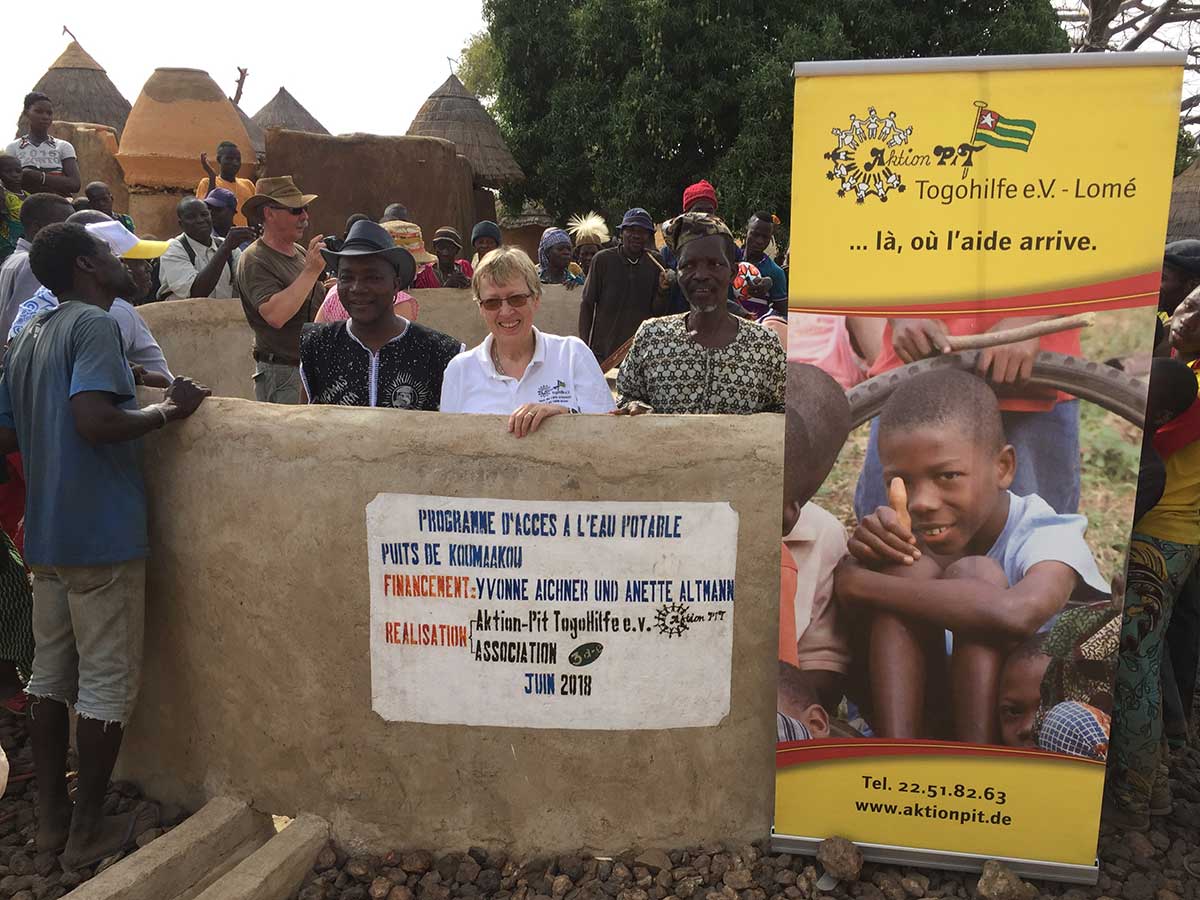 Der Brunnen mit Schild des Spenders v.l.: Mr. Kouagou (unser Partner vor Ort), Margret Kopp, der Dorfchef