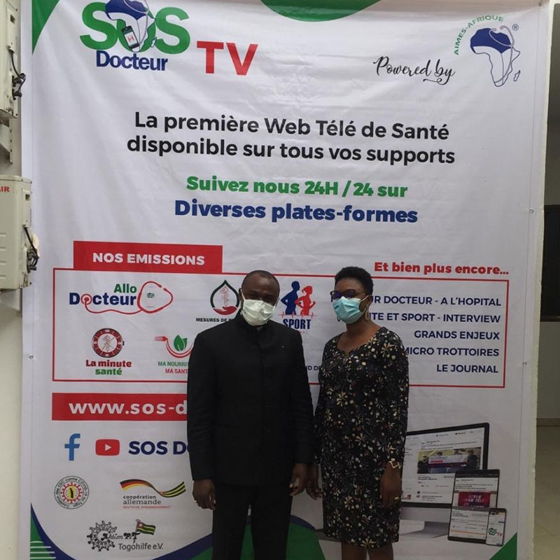 Dr. Kodom mit Elbine Ditoma vor dem großem „SOS Docteur TV“-Banner