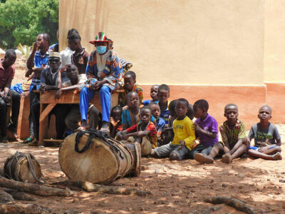 Kinder warten vor einer Schule, im Vordergrund stehen zwei Trommeln