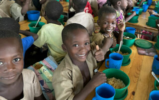 Kinder beim essen, lachen in die Kamera und zeigen den Daumen nach oben