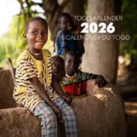 Ein lachender Junge sitzt auf einer Lehmmauer.